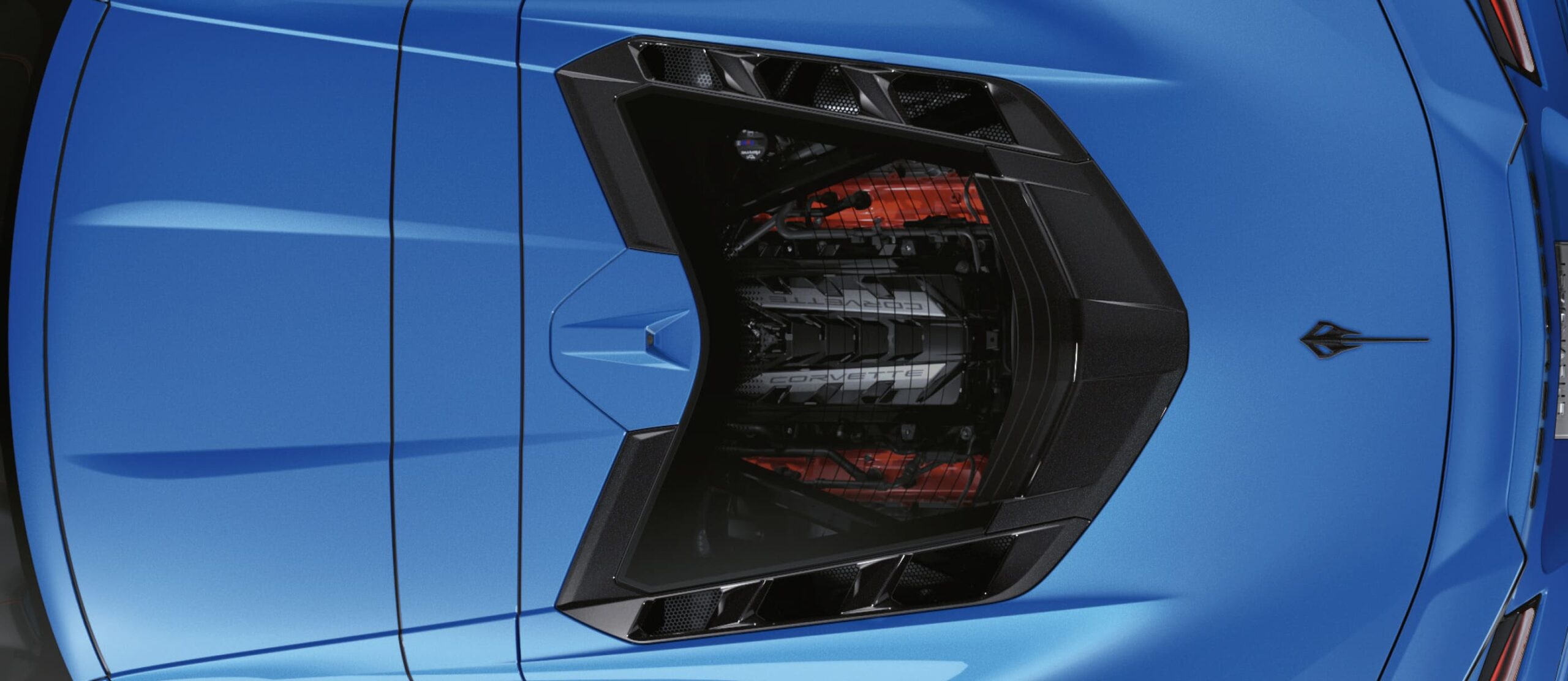 Draufsicht auf den Motorraum einer blauen Chevrolet Corvette E-Ray mit sichtbarem V8-Motor unter einer transparenten Abdeckung
